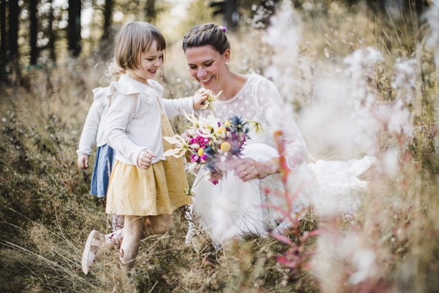 Braut mit ihren Töchtern auf einer Blumenwiese in der Hocke sitzend