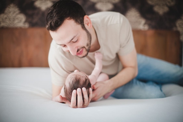 Vater liegt auf dem Bett und hält den Kopf von seinem Baby in seinen Händen