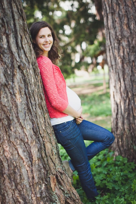 Schwangere Frau lehnt sich an einem Baum an