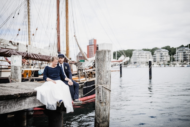 Hochzeitspaar sitzt auf Steg am Hafen