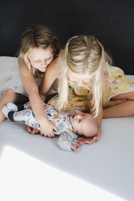 Schwester beugen sich zu ihrem Neugeborenen Geschwisterchen