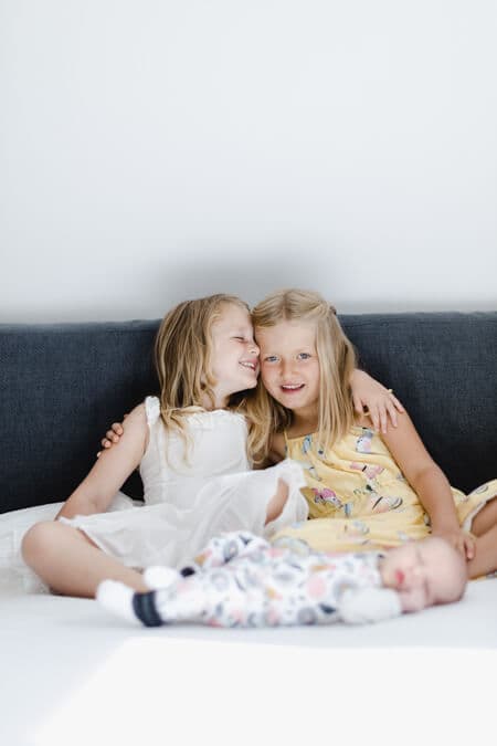 Schwestern sitzten auf dem Bett im Vordergrund liegt ein Neugeborenes