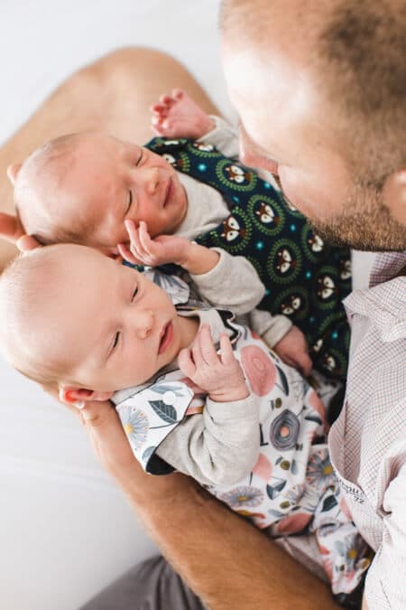 Blick von oben auf Zwillinge die in den Händen vom Vater liegen