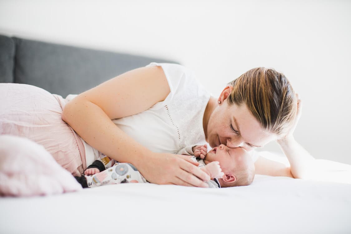 Mutter kuschelt auf dem Bett liegend mit ihrem Baby