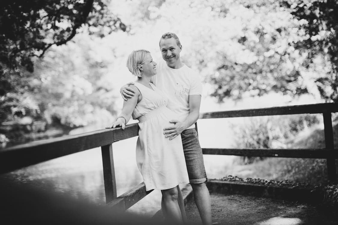 Schwangeres Paar steht am Geländer am See