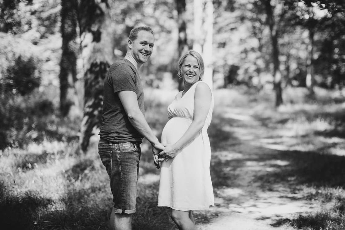 Paar hält sich an den Händen und schaut über die Schulter in die Kamera. Die Frau hat einen Babybauch.