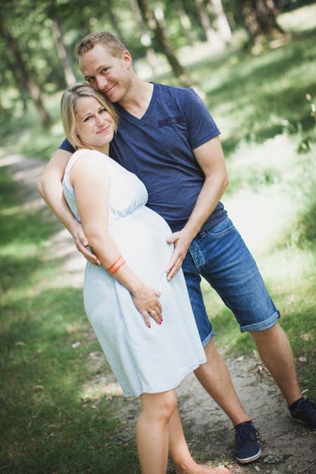 Frau mit einem Babybauch und ihrem Mann zusammen im Grünen