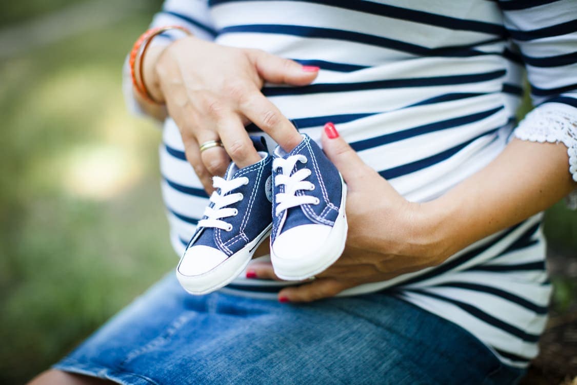 Nahaufnahme von Babybauch mit Babyschuhen in der Hand