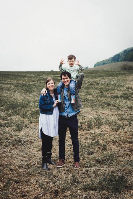 Familie steht auf einem Acker. der Sohn sitzt auf den Schultern des Vaters.