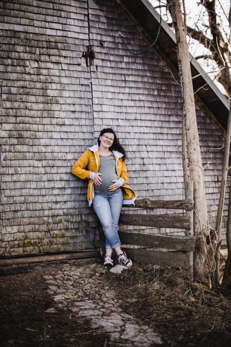 Schwangere Frau lehnt an einer Scheune