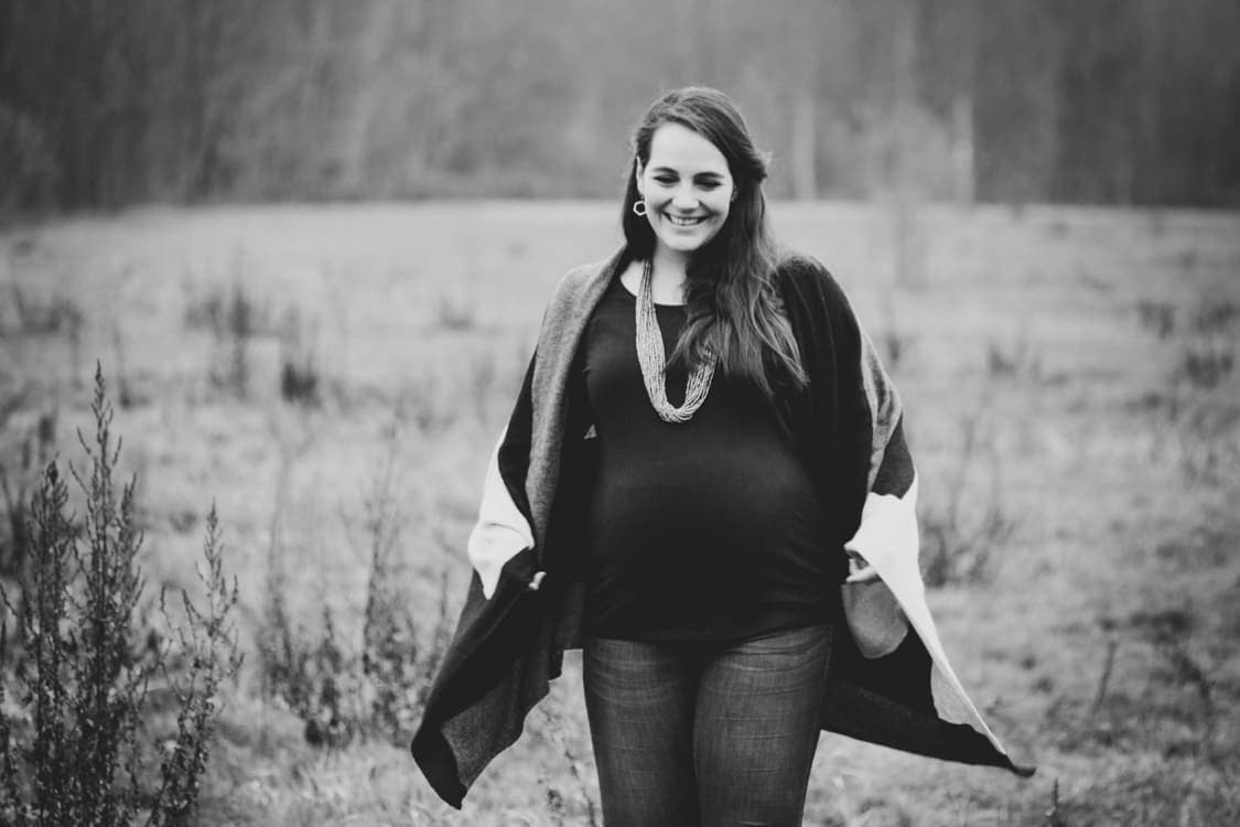 Schwangere Frau mit Strickmantel läuft über Wiese