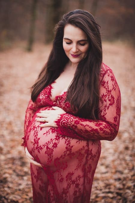 Schwangere Frau im roten Spitzenkleid und langen braunen Haaren