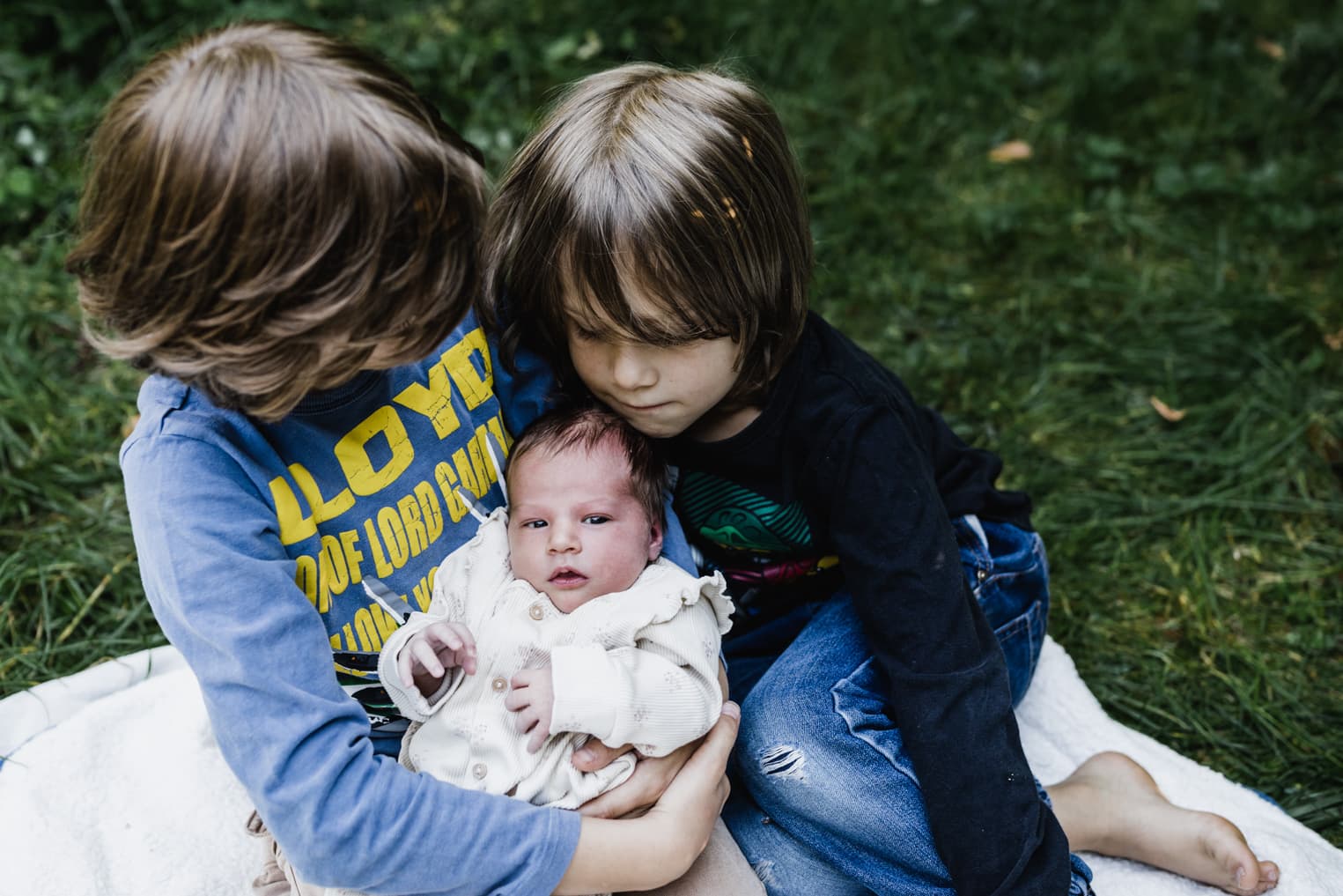 Baby mit Brüdern auf einer Decke im Garten