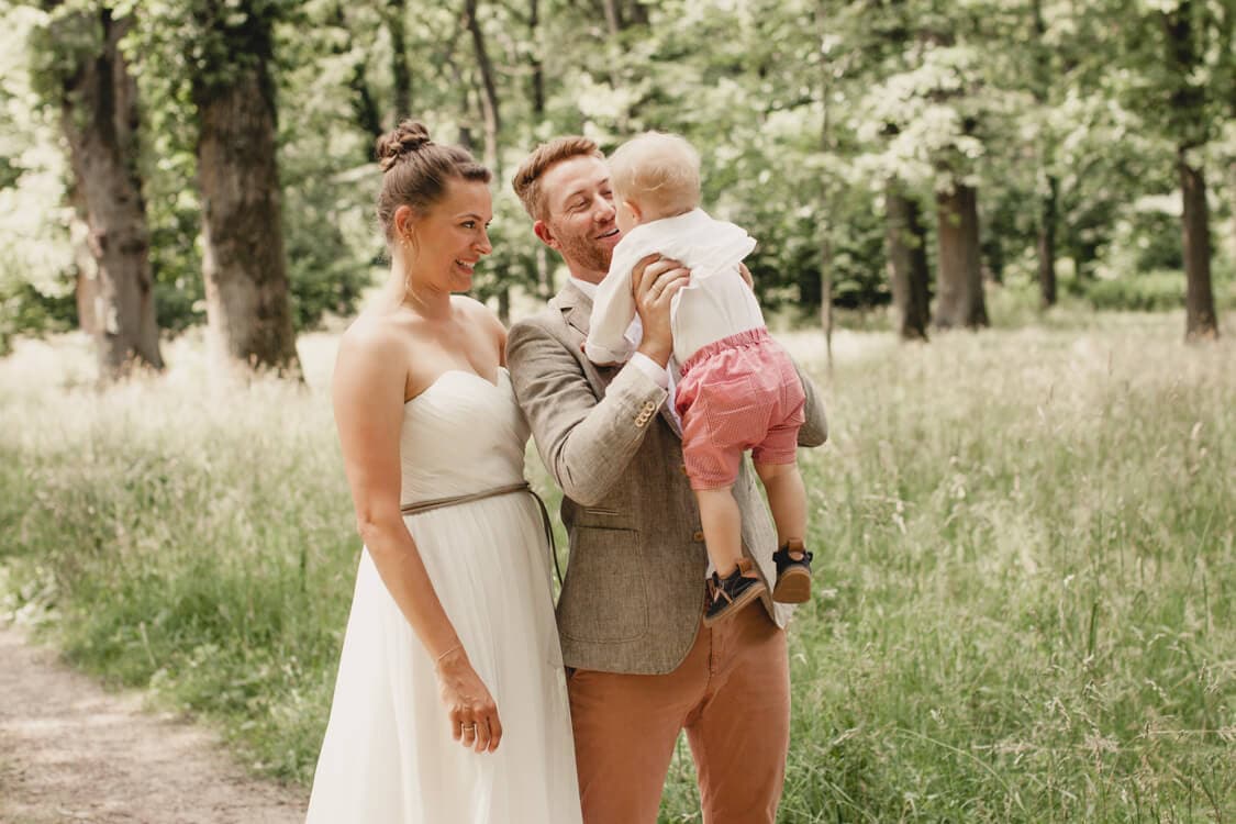 Brautpaar blickt zu ihrem Sohn den der Vater vor sich hoch hebt