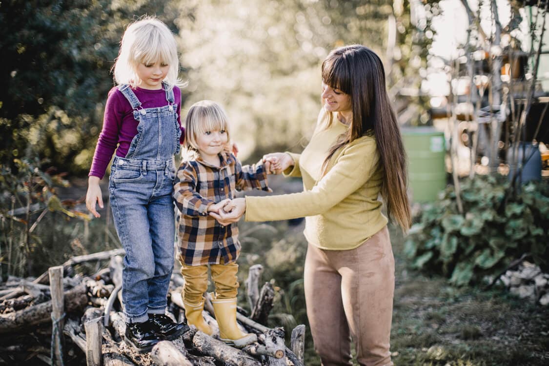 Kinder balancieren auf Ästen. Die Mutter hält sie an den Händen fest.