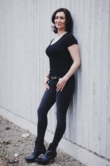 Frau mit schwarzer Hose und schwarzem T-Shirt lehnt an einer Wand