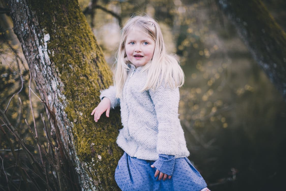 Mädchen leht an einem Baumstamm und blickt über die Schulter