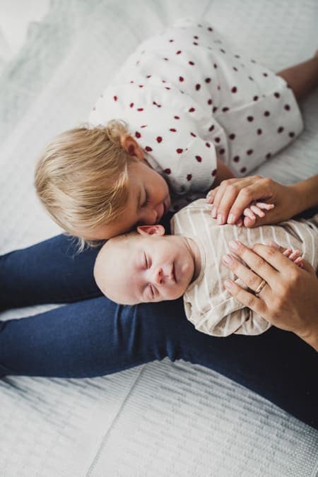 Schwester kuschelt mit kleinem Bruder der auf dem Schoß der Mutter liegt