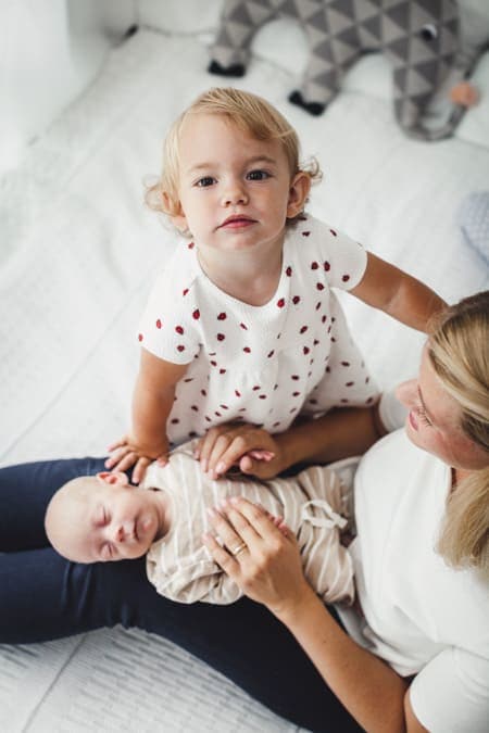 Mädchen blickt hoch in die Kamera und der kleine Bruder liegt auf dem Schoß der Mutter