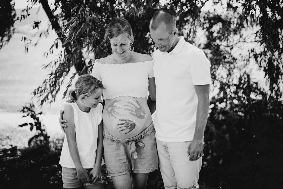 Familie schaut auf Babybauch der Mutter mit Handabdrücken