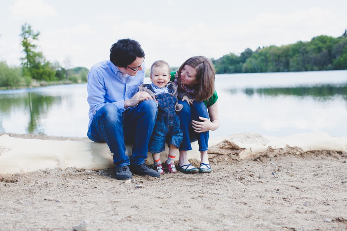 Kleine Familie sitzt auf Baumstamm am See