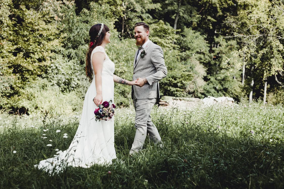 Brautpaar auf eiiner Wiese. Der Bräutigam streckt nach der Braut die Hand aus die ihm gegenüber steht.