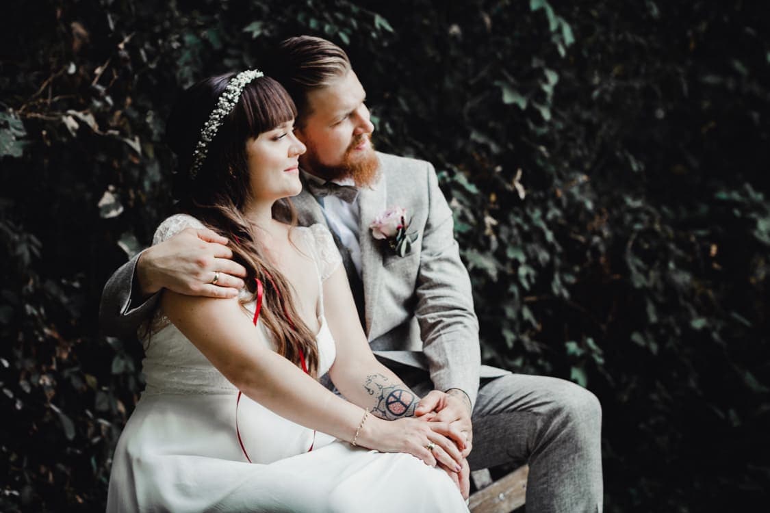 Brautpaar sitzt auf der Lehne einer Bank und blickt in die Ferne