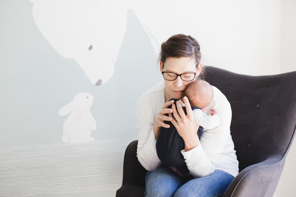 Mutter kuschelt ihr Baby vor Kinderzimmerwand