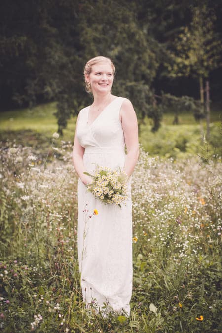 Braut in Blumenwiese und Brautstrauß in der Hand