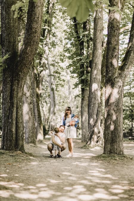 Familie in einer Allee von Bäumen. Kind rennt dem Vater in die Arme.