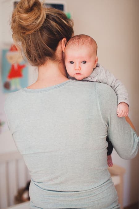 Baby auf dem Arm blickt über die Schulter der Mutter