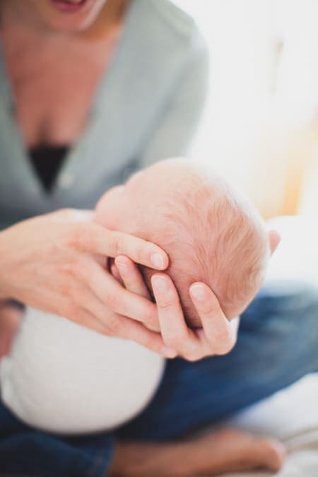 Nahaufnahme von dem Köpfchen des Babys in den Händen der Mutter