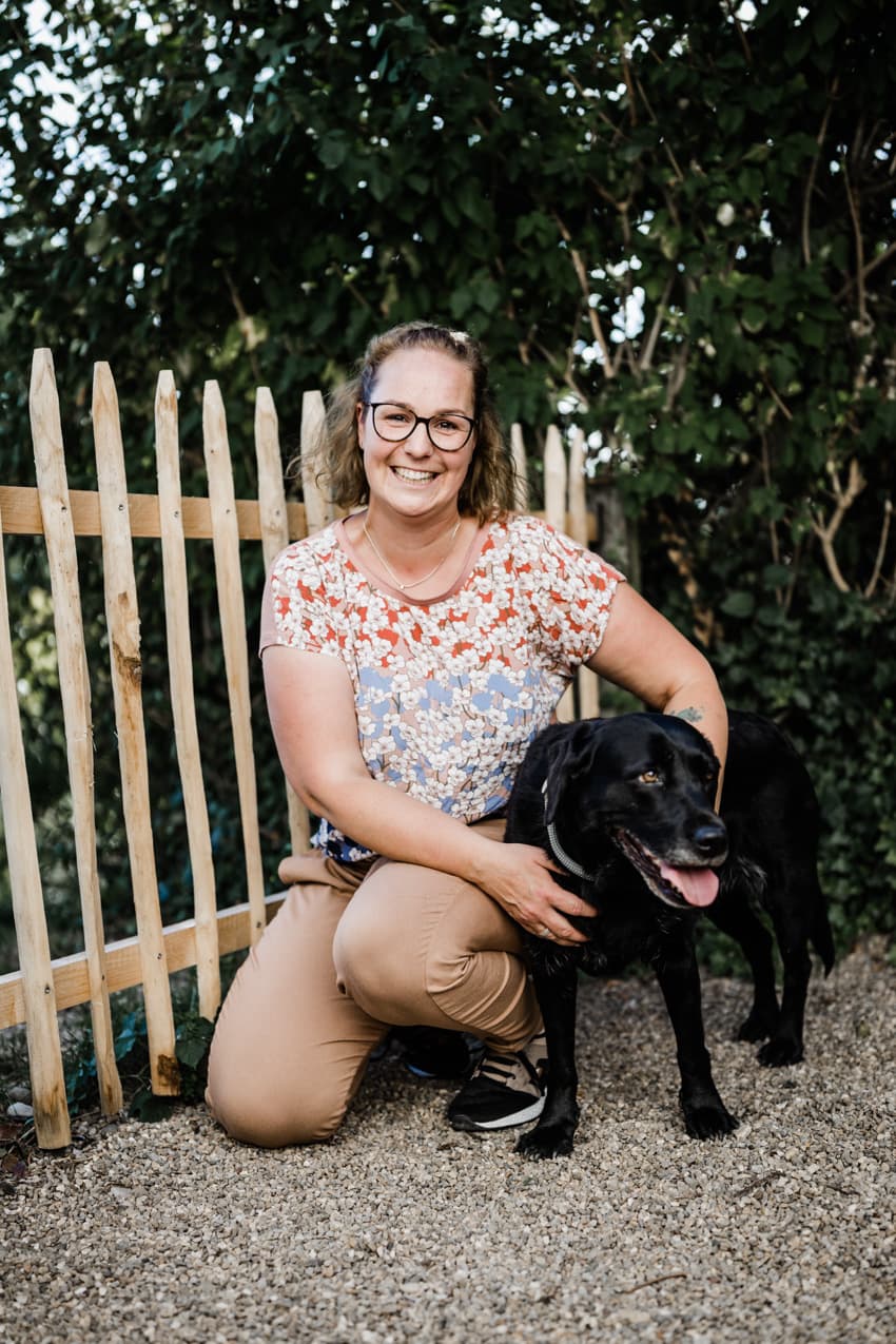 Frau mit Hund am Gartenzaun sitzend