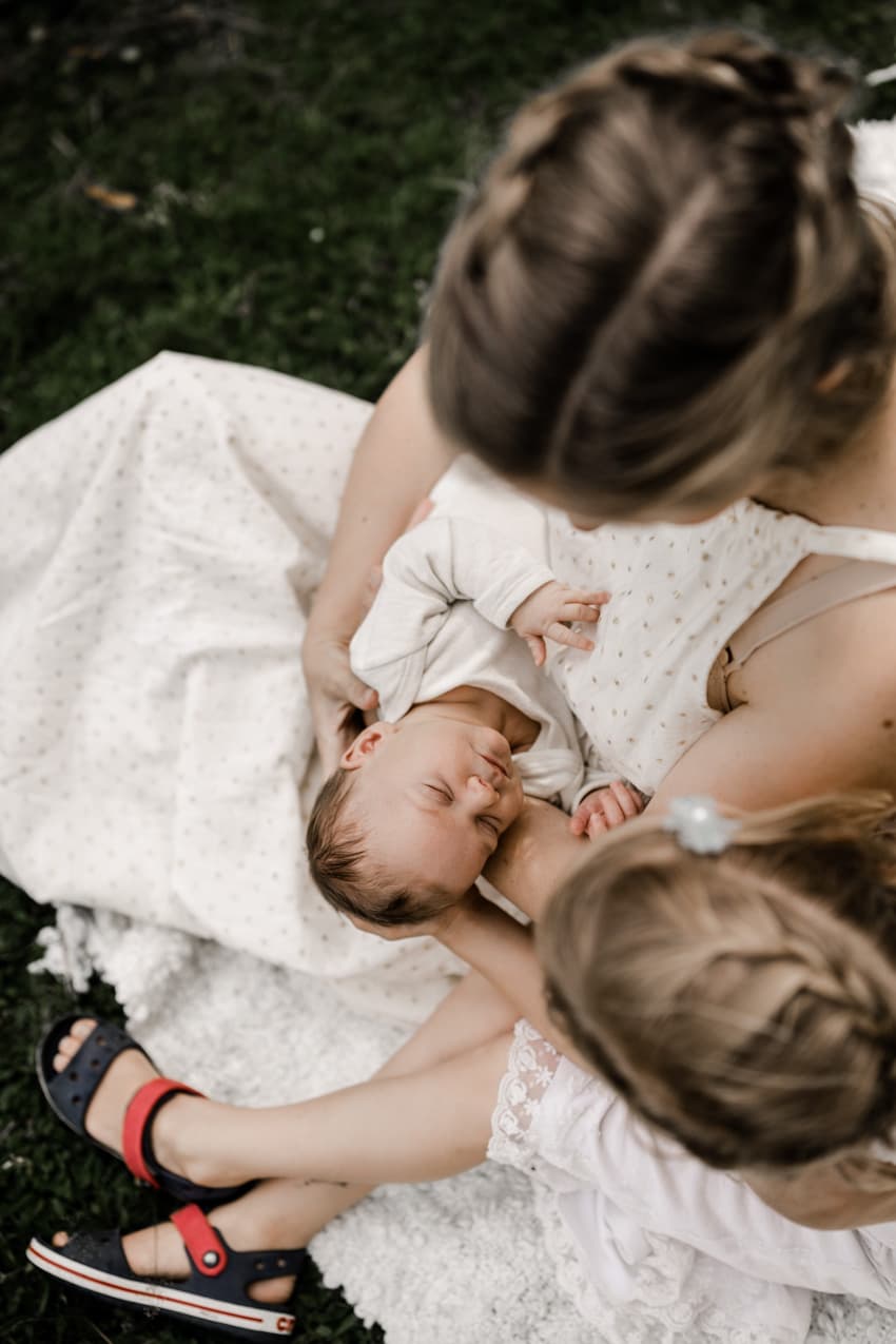 Baby schläft auf dem Arm der Mutter und Schwester sitzt nebendran