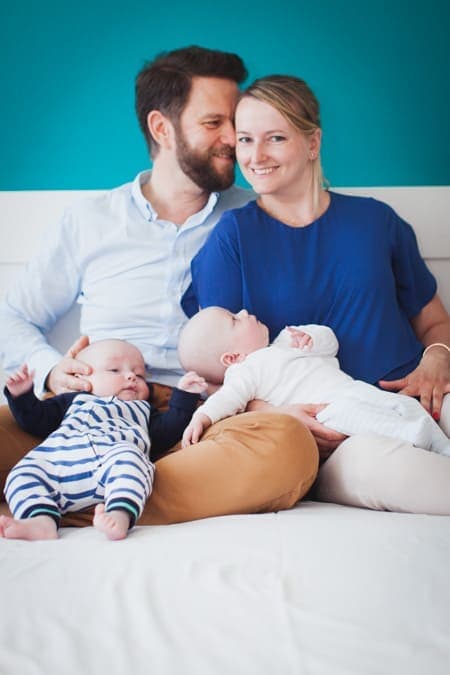 Eltern sitzen mit ihren Zwillingsbabys auf dem Bett und kuscheln