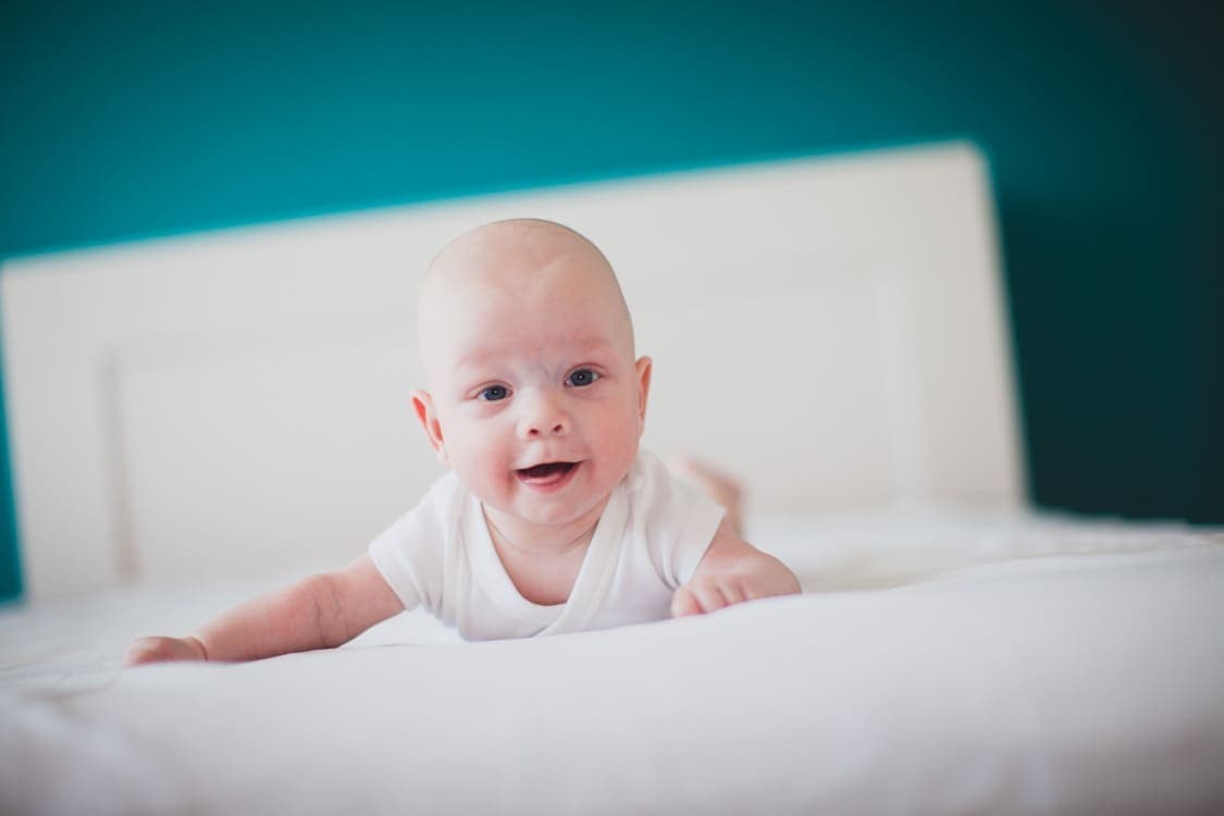 Baby liegt auf dem Bauch auf einem Bett und lacht