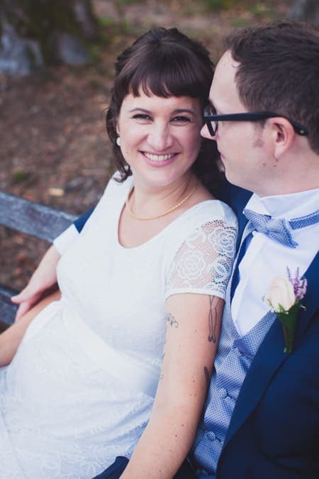 Nahaufnahme von einer Braut die auf einer Bank sitzt in den Armen des Bräutigams