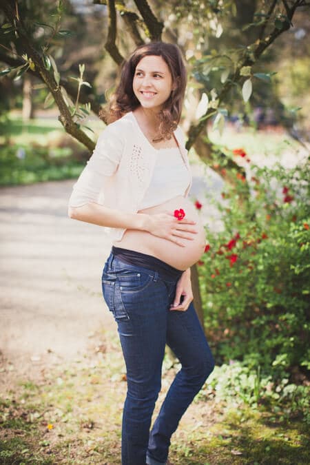 Schwangere Frau hält Blume auf ihren Babybauch