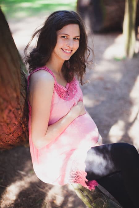 Schwangere Frau sitzt auf einem Ast und blickt in die Kamera