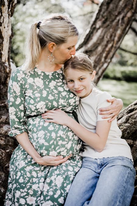 Mutter mit Babybauch gibt Tochter einen Kuss