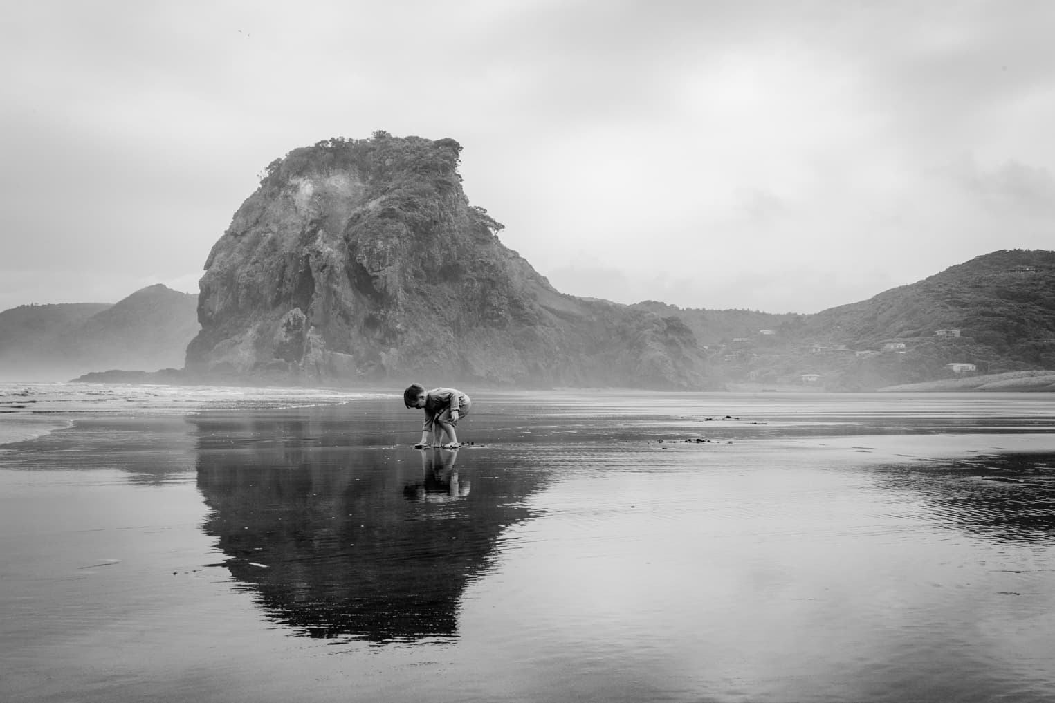 Junge am Strand. Felsen spiegeln sich im Wasser.