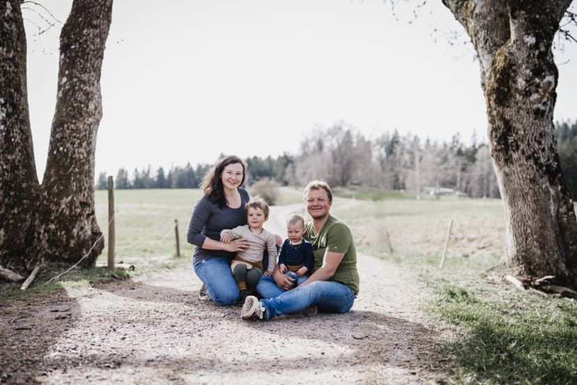 Familie sitzt auf einem Weg zwischen zwei Baeumen