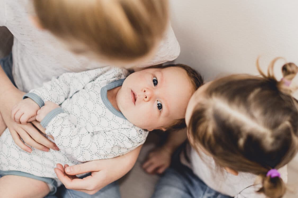 Schwestern halten ihren kleinen Bruder auf dem Schoß. Blick von oben auf das Baby.