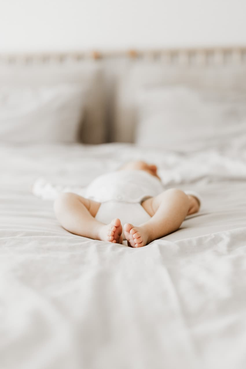 Baby liegt in einem Body auf dem Bett beim professionellen Neugeborenen-Shooting