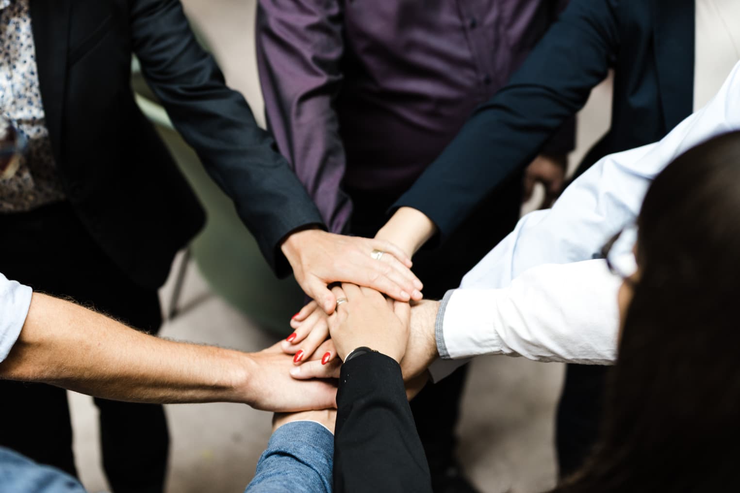 Teambild in der Unternehmensfotografie, Mitarbeitende legen Hände übereinander als Symbol für Zusammenarbeit