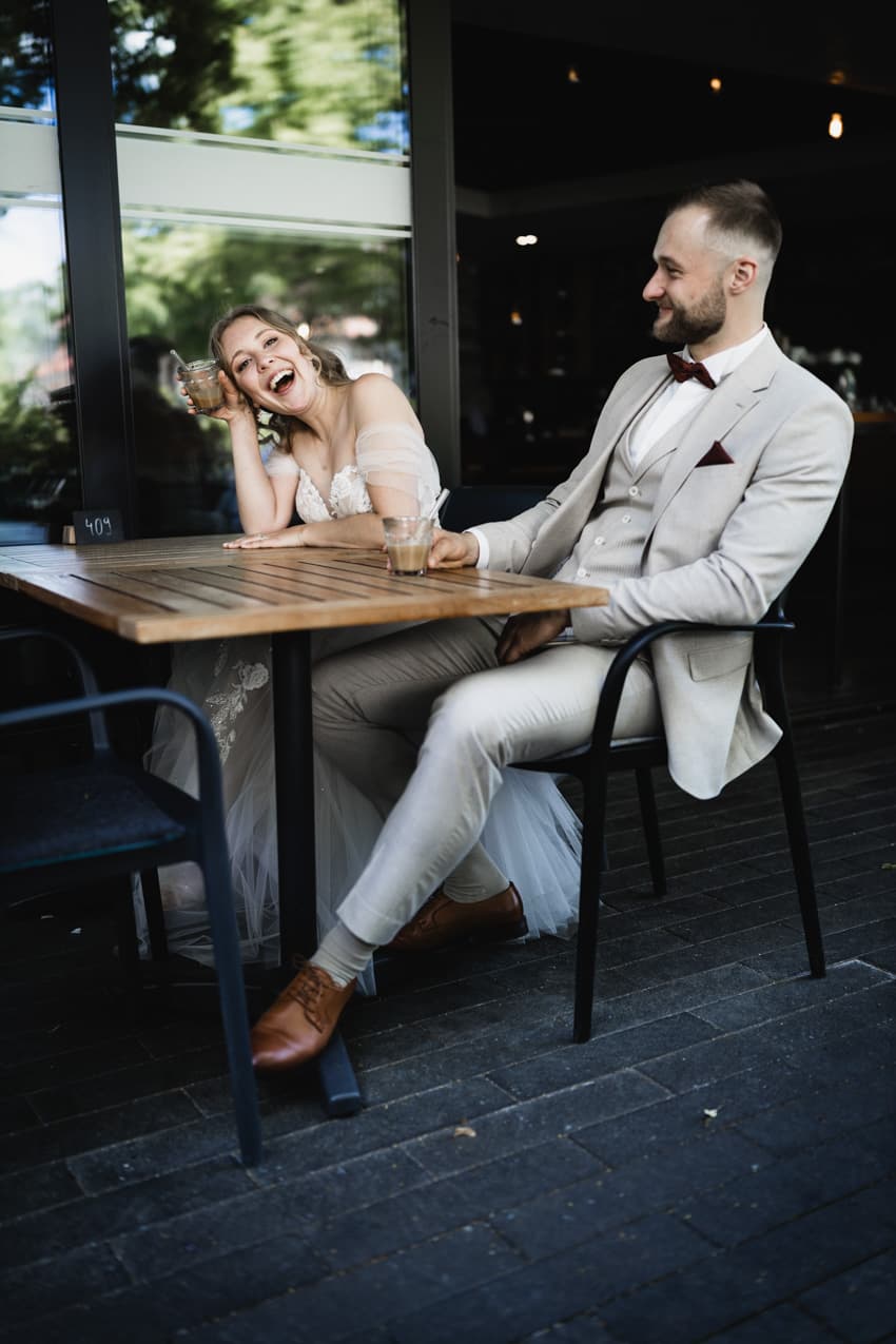 Braut lacht, hält Kaffee, Bräutigam sitzt daneben natürliche Hochzeitsfotografie