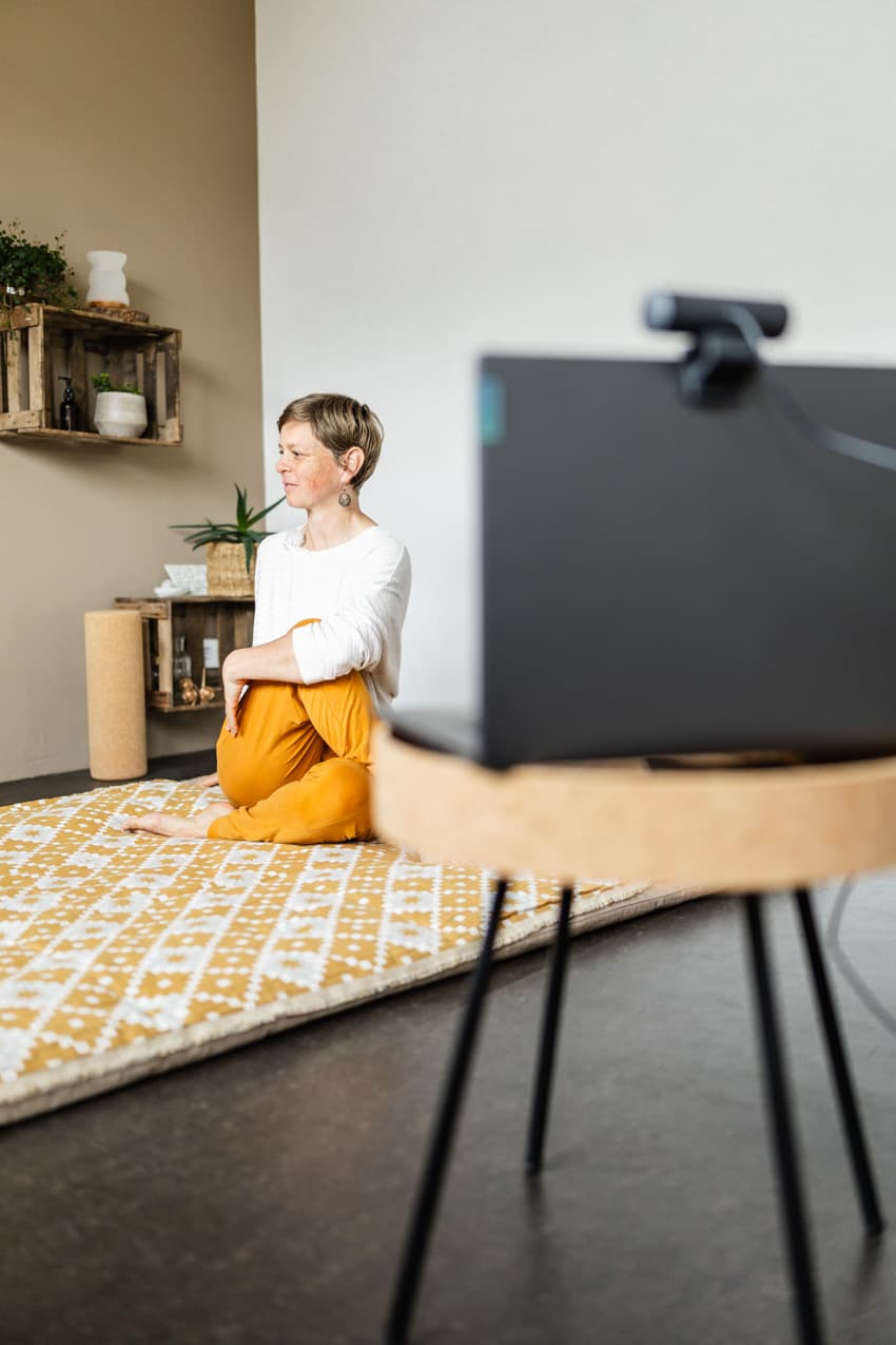 Frau macht Yogaübung vor dem Laptop im Studio, dynamische und natürliche Business-Fotos