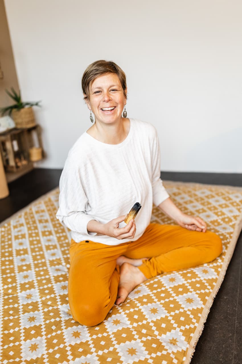 Lachende Yogalehrerin hält Räucherstäbchen im Studio, natürliche Business-Aufnahme