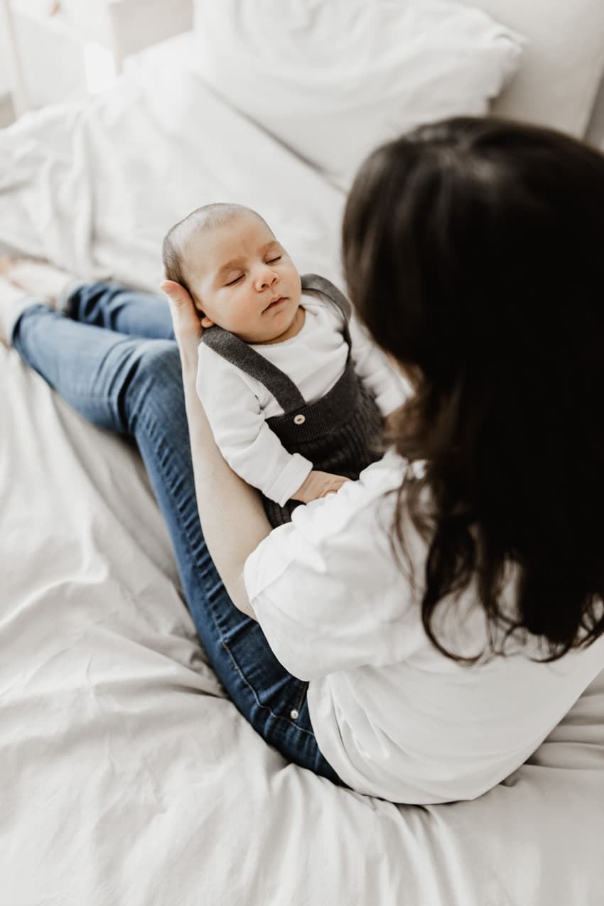 Mutter hält ihr Baby auf dem Schoß sitzend auf dem Bett, entspannte Aufnahme