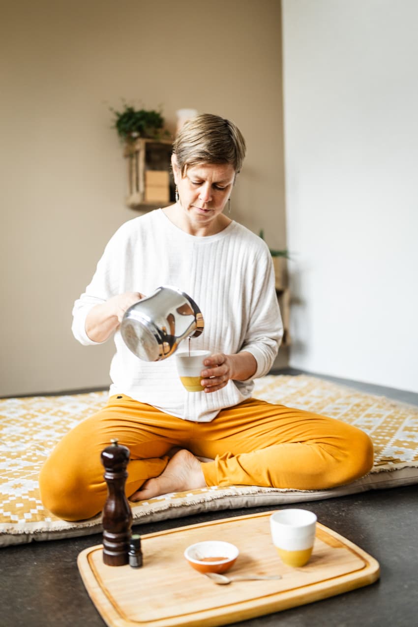 Frau gießt Cacao in Tasse, sitzt debei im Schneidersitz, natürliche Business-Fotografie